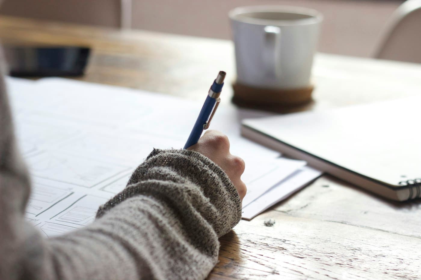 Someone filling in printed worksheets at a desk, coffee within reach